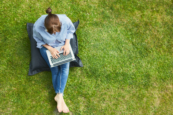 Woman as a freelancer on the laptop PC in the summer in the green garden on the meadow from above