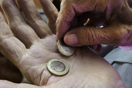 Zwei 1-Euro-Stücke sind in der geöffneten Hand mit deutlichen Falten zu sehen