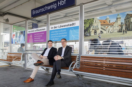 Oberbürgermeister Dr. Thorsten Kornblum und Gerold Leppa, Geschäftsführer des Stadtmarketings, präsentieren die neuen Beklebungen an den Sitzeinhausungen am Hauptbahnhof.
