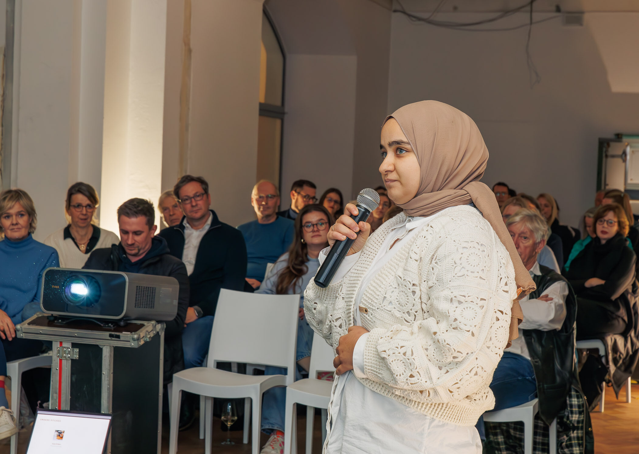 Das Bild zeigt eine Frau, die vor einer Gruppe Menschen spricht. (Wird bei Klick vergrößert)