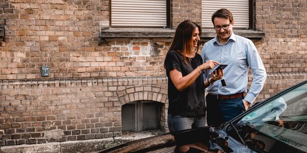 Eine Frau und ein Mann stehen mit einem Smartphone in der Hand am Auto (Wird bei Klick vergrößert)